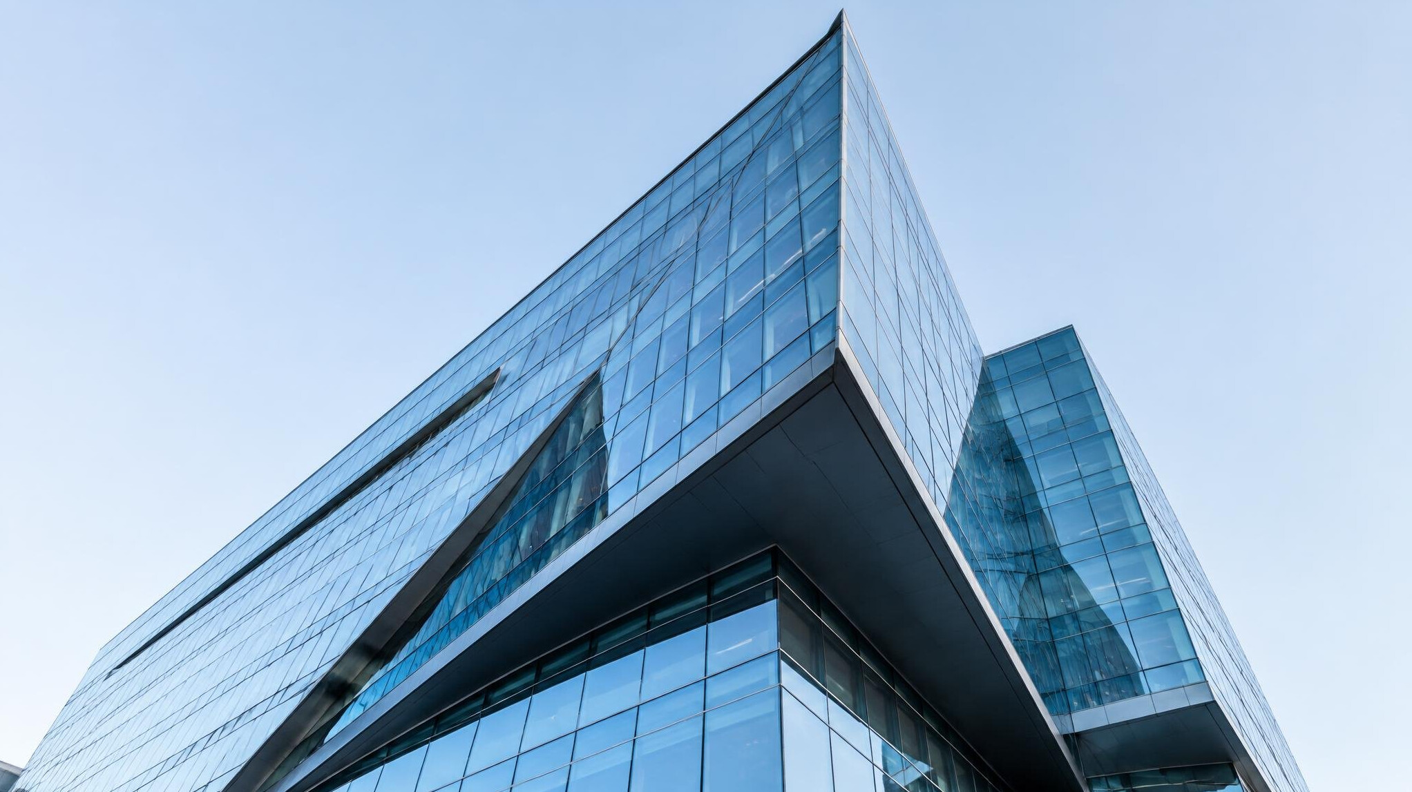 Modern glass office building with angular architecture against a clear sky